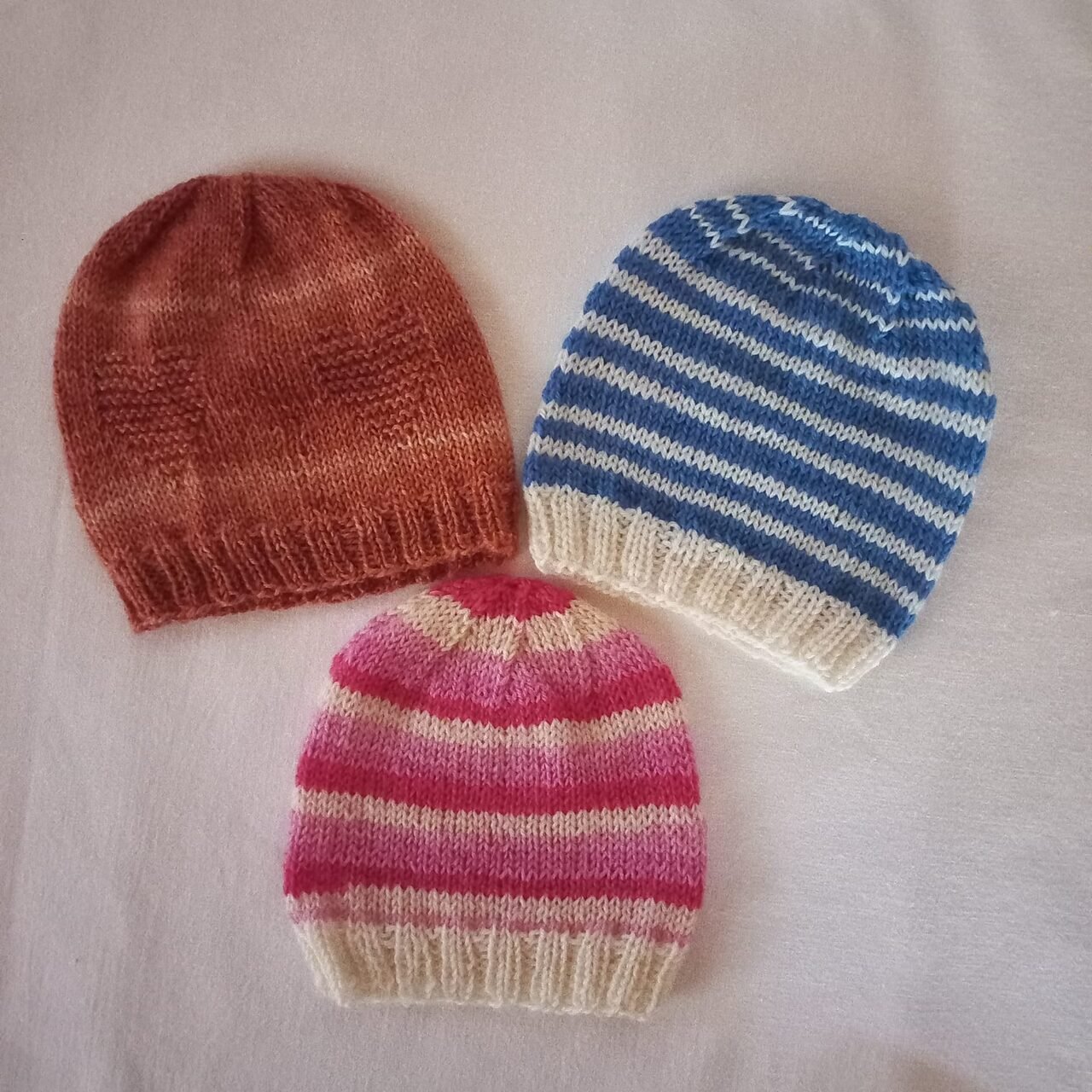 Drei handgestrickte Babymützen in verschiedenen Farben